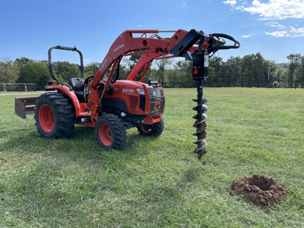 Kubota L4701 HST with loader-mounted auger on the property